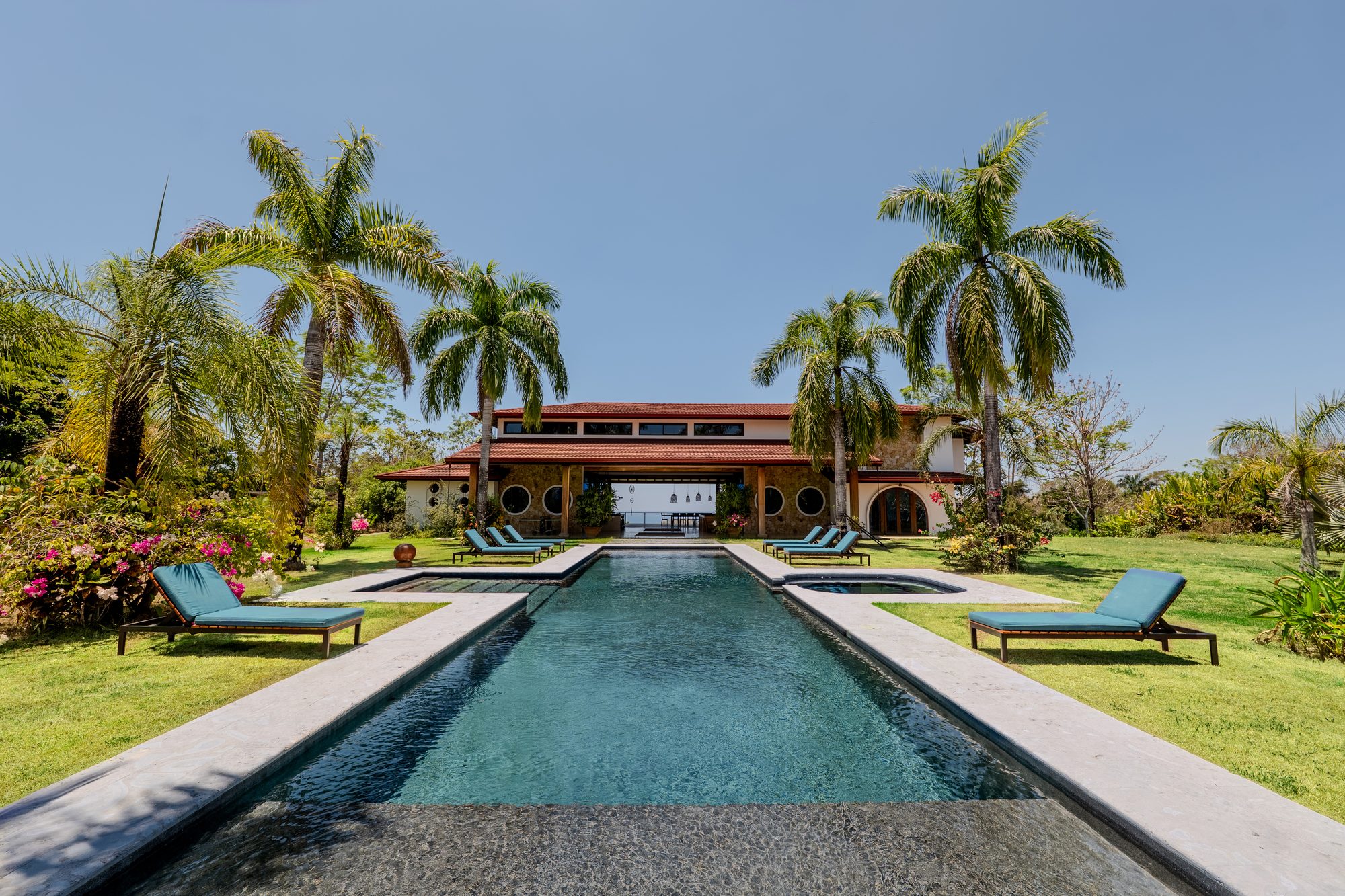 Tanit Villa's 18-metre pool lined with loungers and royal palms, the stone-and-tile house beyond