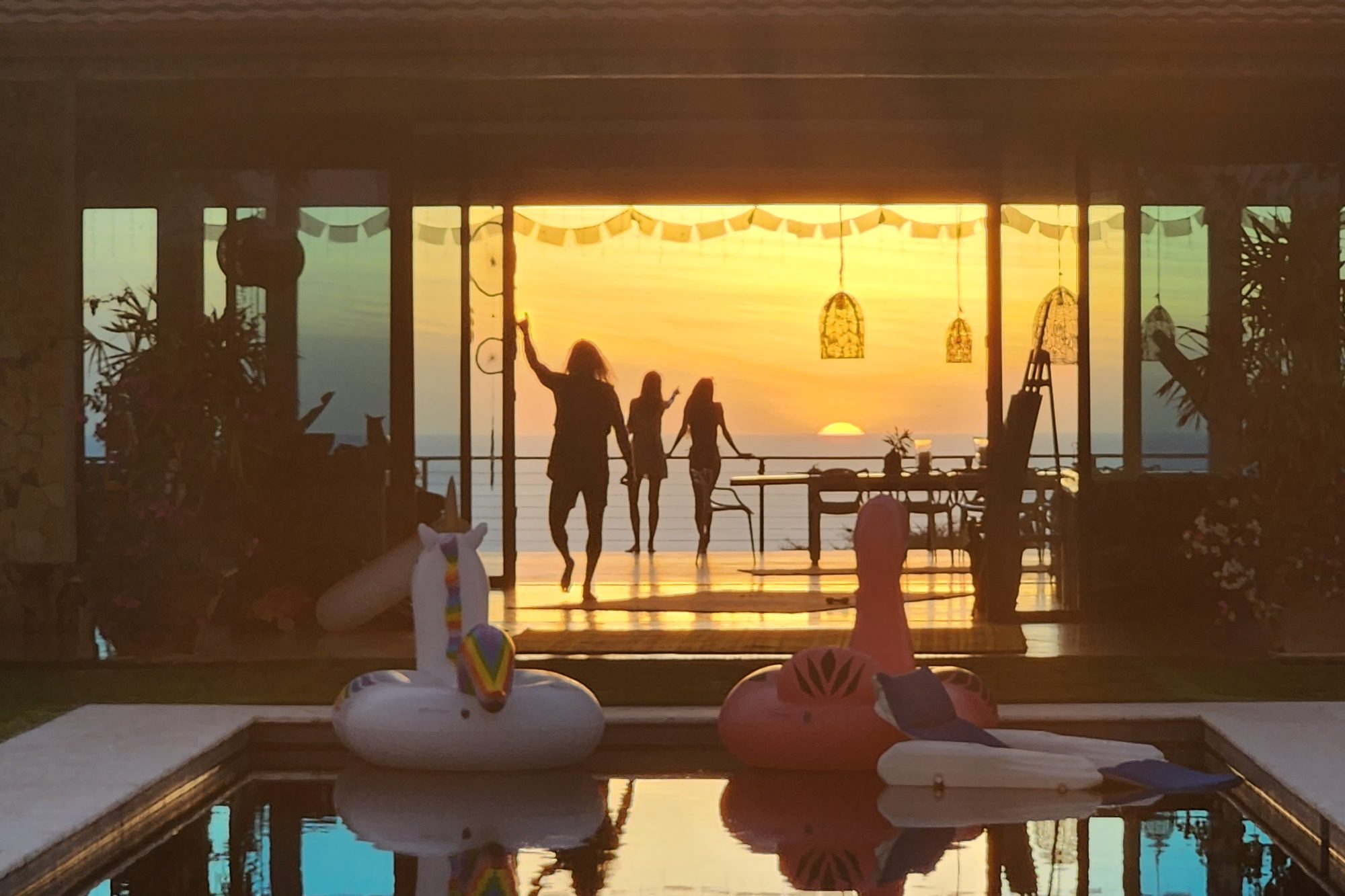 Guests celebrating on the villa's deck at sunset over the Pacific, seen across the pool